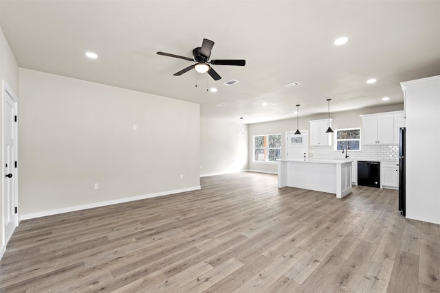 unfurnished living room featuring ceiling fan, sink, and light wood-type flooring