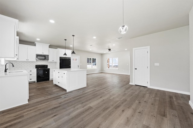 kitchen with black range with electric stovetop, hanging light fixtures, fridge, white cabinets, and a kitchen island