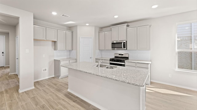 kitchen featuring light stone counters, stainless steel appliances, a kitchen island with sink, sink, and light hardwood / wood-style floors