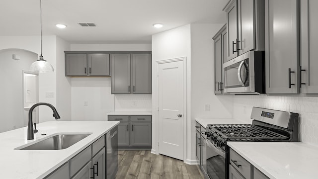 kitchen with pendant lighting, sink, gray cabinetry, backsplash, and stainless steel appliances