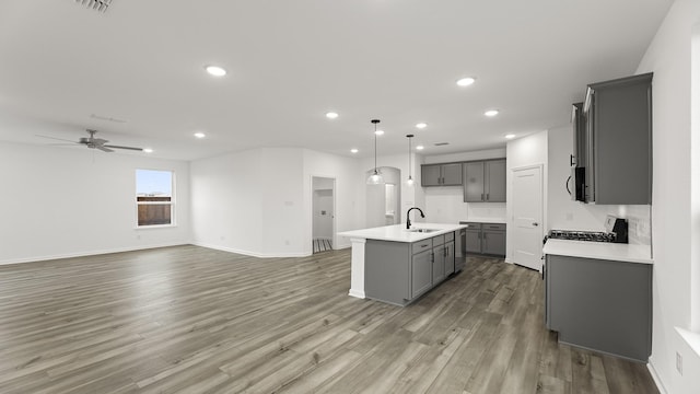 kitchen featuring sink, gray cabinetry, a center island with sink, pendant lighting, and hardwood / wood-style floors