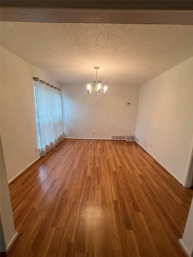 spare room with hardwood / wood-style floors, a textured ceiling, and a notable chandelier