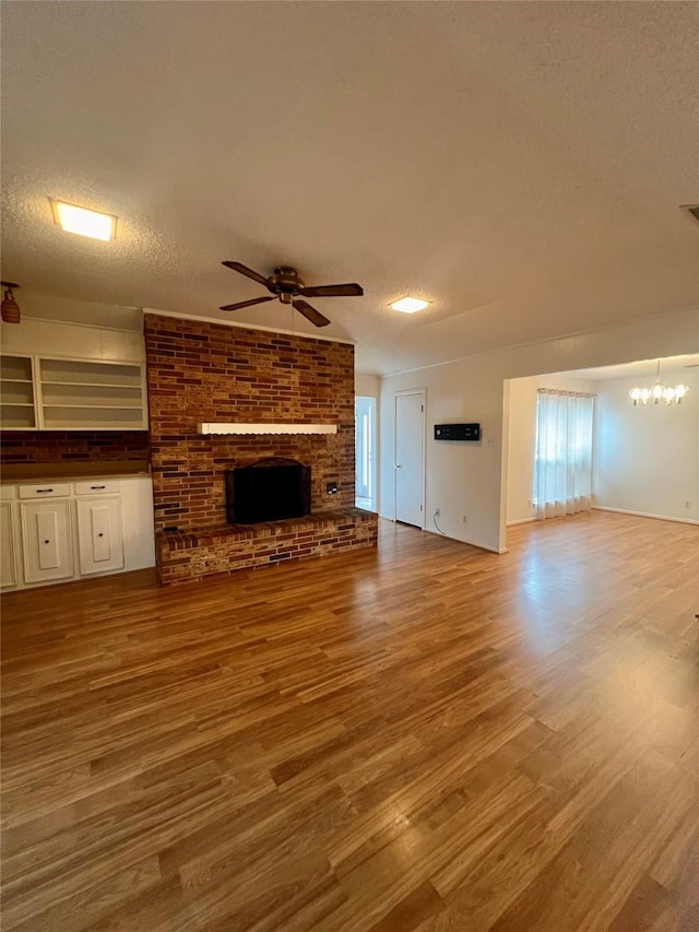 unfurnished living room with ceiling fan with notable chandelier, a textured ceiling, hardwood / wood-style flooring, and a brick fireplace