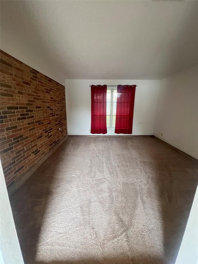 unfurnished room featuring lofted ceiling, carpet, and brick wall