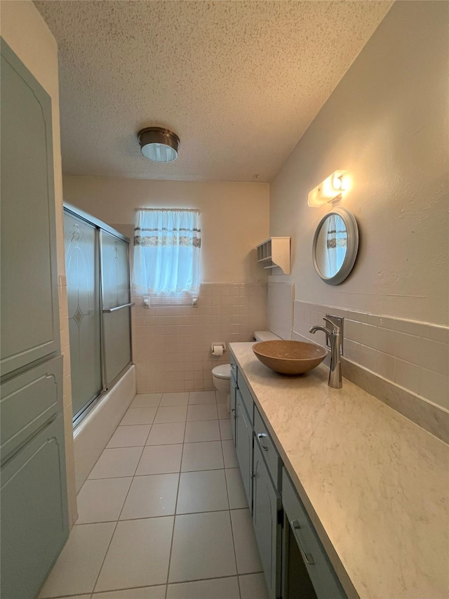 full bathroom with enclosed tub / shower combo, tile patterned floors, a textured ceiling, vanity, and tile walls