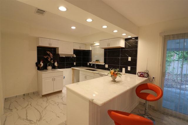 kitchen featuring kitchen peninsula, backsplash, a breakfast bar, sink, and white cabinetry