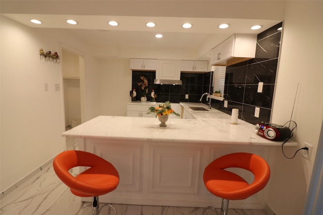 kitchen featuring kitchen peninsula, a kitchen bar, tasteful backsplash, and white cabinetry