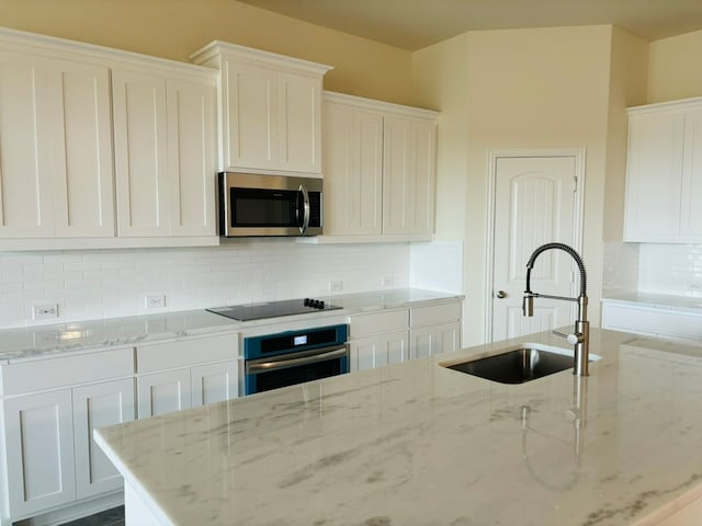 kitchen with white cabinetry, stainless steel appliances, light stone countertops, and sink