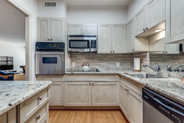 kitchen with light stone countertops, light wood-type flooring, tasteful backsplash, stainless steel appliances, and sink