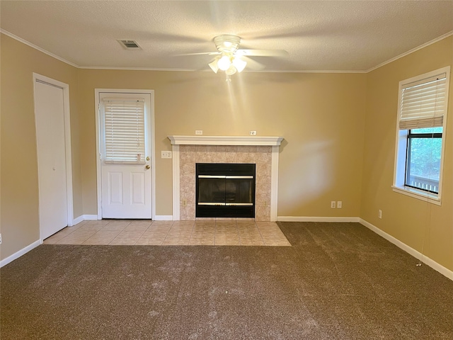 unfurnished living room featuring a tile fireplace, light colored carpet, ceiling fan, crown molding, and a textured ceiling