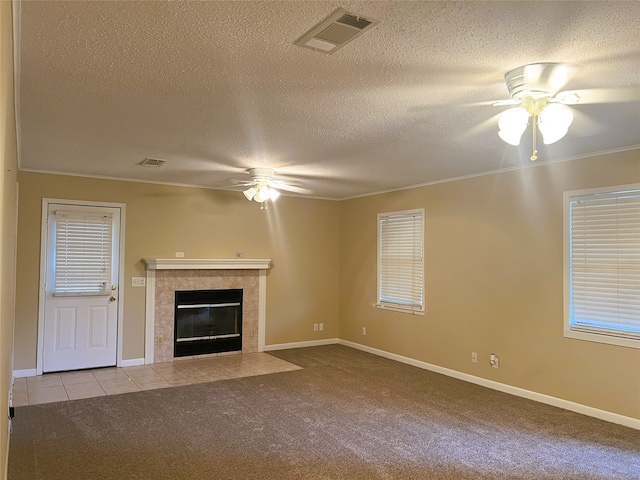 unfurnished living room with light colored carpet, a textured ceiling, ornamental molding, ceiling fan, and a tiled fireplace