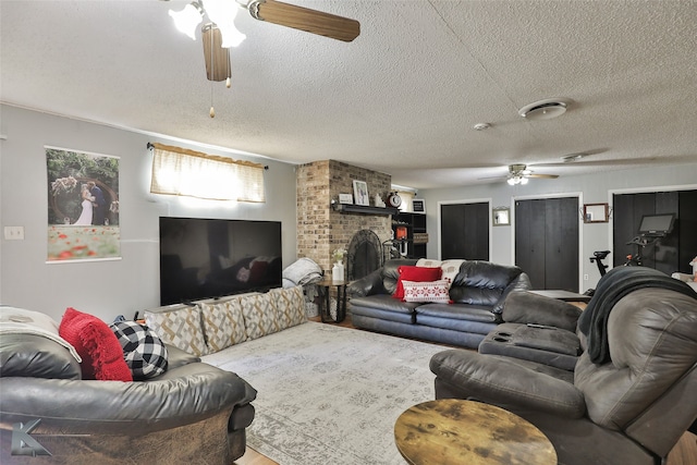 living room with a textured ceiling, a brick fireplace, and ceiling fan