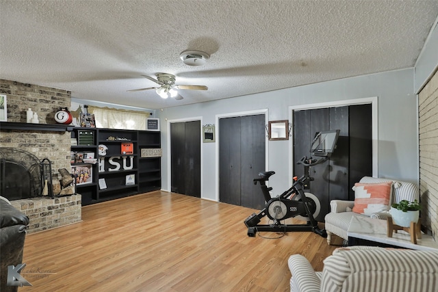 workout room with ceiling fan, brick wall, a textured ceiling, a fireplace, and hardwood / wood-style flooring