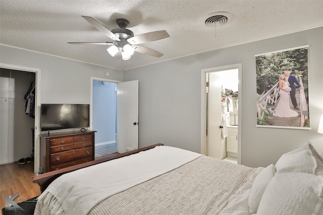 bedroom with ceiling fan, ensuite bathroom, a textured ceiling, a closet, and hardwood / wood-style flooring