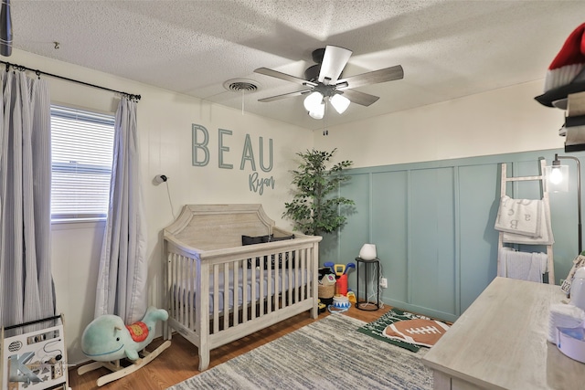 bedroom featuring a textured ceiling, ceiling fan, dark hardwood / wood-style floors, and a crib