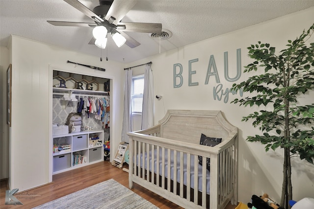 bedroom with a textured ceiling, ceiling fan, a crib, and hardwood / wood-style flooring