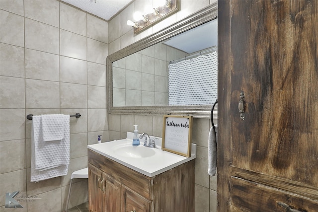 bathroom with a textured ceiling, vanity, and tile walls