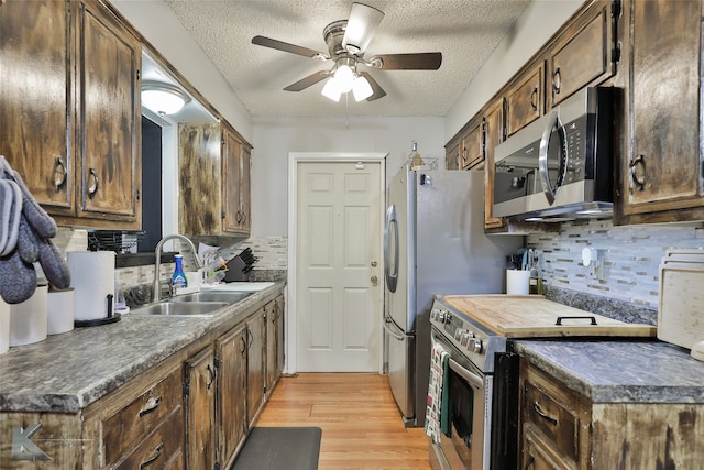 kitchen featuring sink, decorative backsplash, light wood-type flooring, a textured ceiling, and appliances with stainless steel finishes