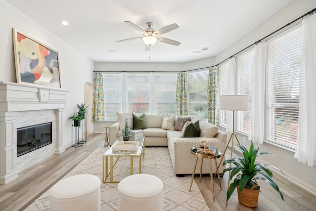 living room featuring light wood-type flooring, baseboards, a ceiling fan, and a tile fireplace