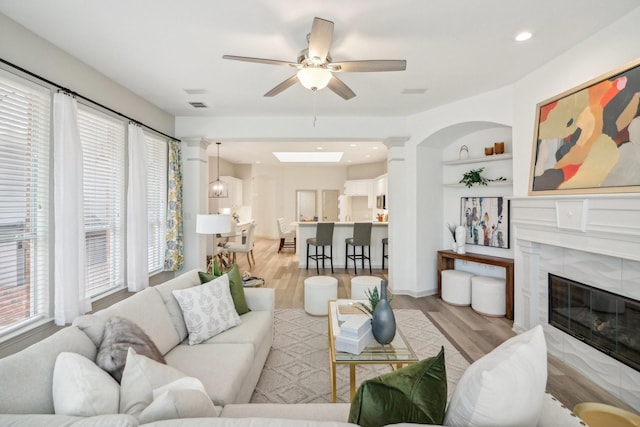 living area with ceiling fan, built in shelves, a fireplace, visible vents, and light wood-style floors