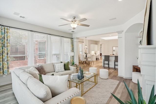 living room with arched walkways, visible vents, light wood-style flooring, a ceiling fan, and baseboards