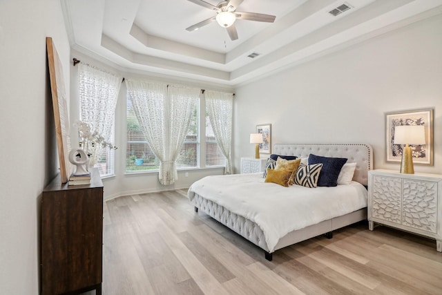 bedroom with light wood finished floors, a tray ceiling, visible vents, and baseboards