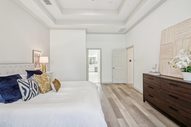 bedroom with a high ceiling, visible vents, baseboards, light wood-type flooring, and a raised ceiling