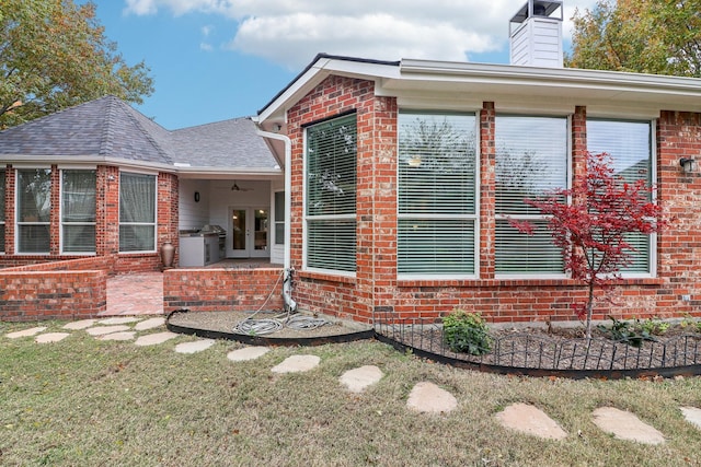 view of property exterior featuring brick siding, a ceiling fan, french doors, roof with shingles, and a chimney