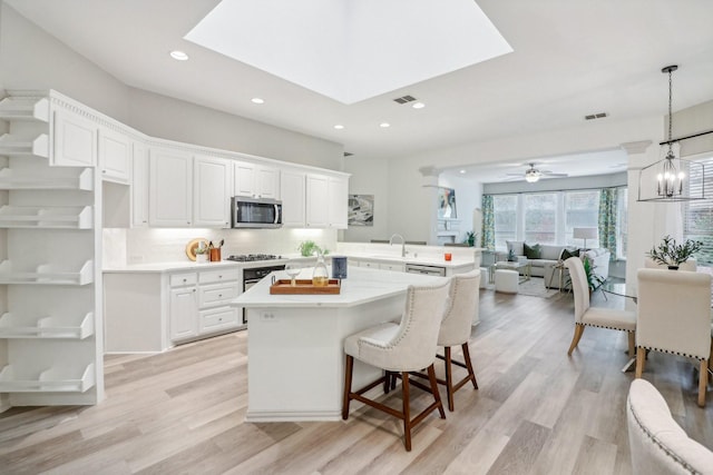 kitchen with light countertops, a skylight, stainless steel microwave, and light wood-style flooring