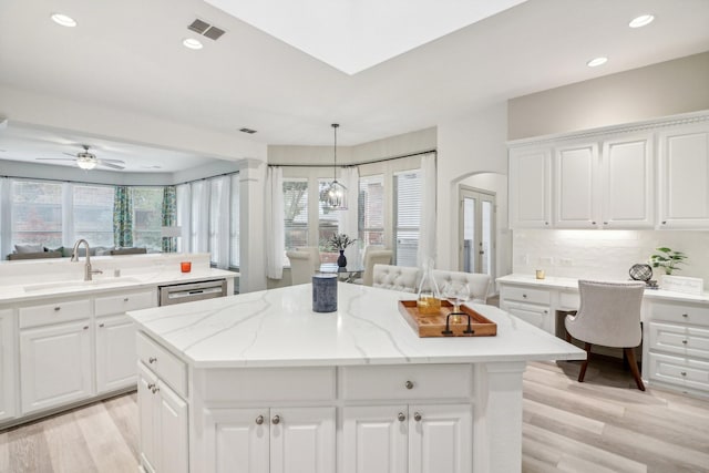 kitchen with built in desk, decorative backsplash, stainless steel dishwasher, a kitchen island, and a sink