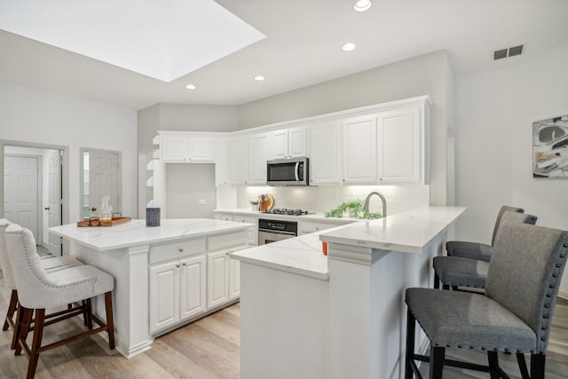 kitchen featuring a breakfast bar area, stainless steel appliances, a skylight, white cabinets, and tasteful backsplash