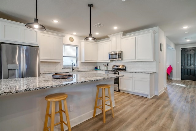 kitchen with stainless steel appliances, white cabinets, and decorative light fixtures