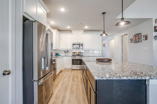 kitchen with a center island, hanging light fixtures, appliances with stainless steel finishes, light stone countertops, and white cabinets