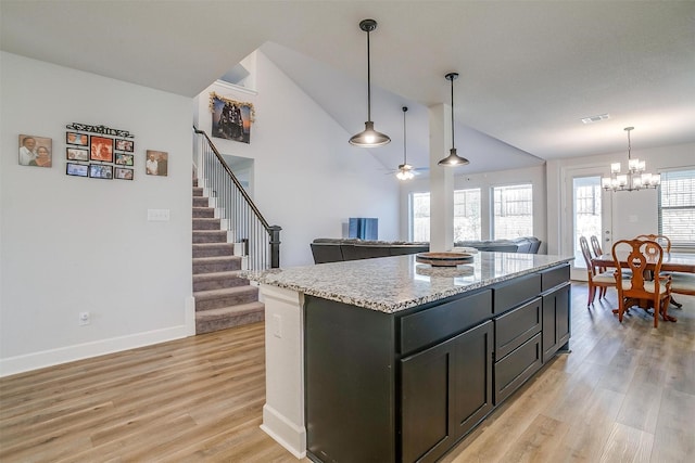 kitchen with a center island, light hardwood / wood-style floors, light stone countertops, decorative light fixtures, and vaulted ceiling