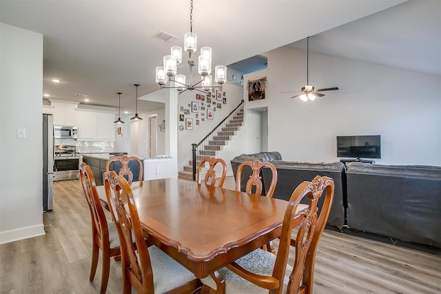 dining space with vaulted ceiling, ceiling fan with notable chandelier, and light hardwood / wood-style floors