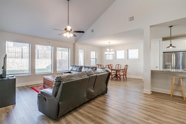 living room featuring high vaulted ceiling, ceiling fan with notable chandelier, and light wood-type flooring