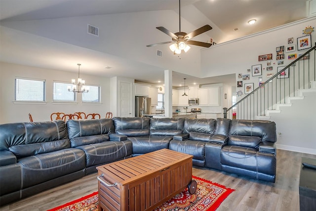 living room featuring high vaulted ceiling, ceiling fan with notable chandelier, and light hardwood / wood-style floors