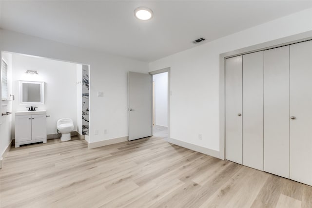 unfurnished bedroom featuring connected bathroom, sink, and light hardwood / wood-style floors