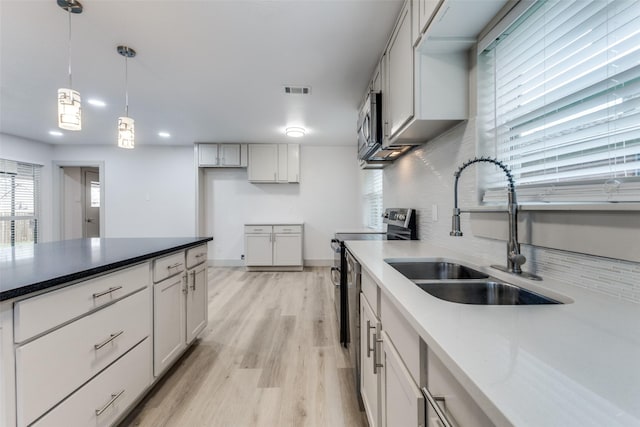 kitchen featuring sink, light hardwood / wood-style flooring, decorative backsplash, decorative light fixtures, and stainless steel appliances