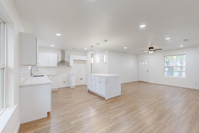 kitchen with wall chimney exhaust hood, a center island, white cabinetry, and light hardwood / wood-style flooring