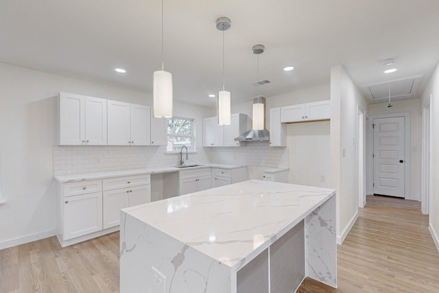 kitchen with a center island, sink, wall chimney range hood, pendant lighting, and white cabinets