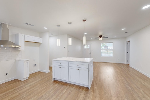 kitchen with ceiling fan, wall chimney range hood, pendant lighting, light hardwood / wood-style flooring, and white cabinetry