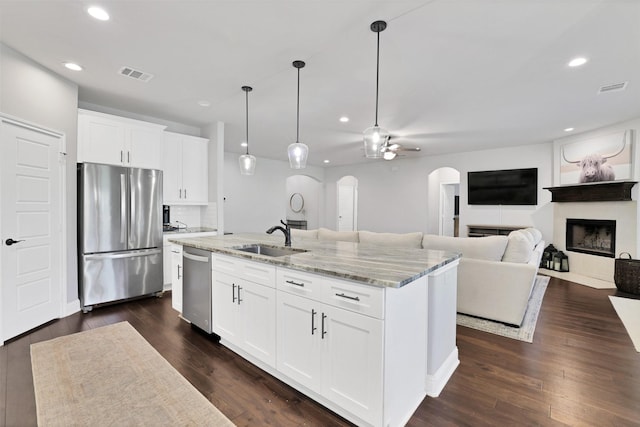 kitchen featuring appliances with stainless steel finishes, light stone counters, ceiling fan, white cabinets, and an island with sink