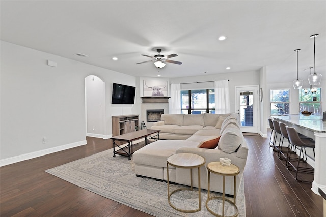 living room with a large fireplace, ceiling fan, and dark wood-type flooring