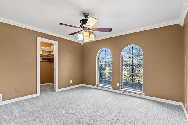 unfurnished bedroom with a spacious closet, crown molding, ceiling fan, and light colored carpet