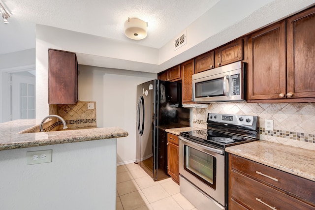 kitchen with appliances with stainless steel finishes, light tile patterned floors, light stone counters, and kitchen peninsula