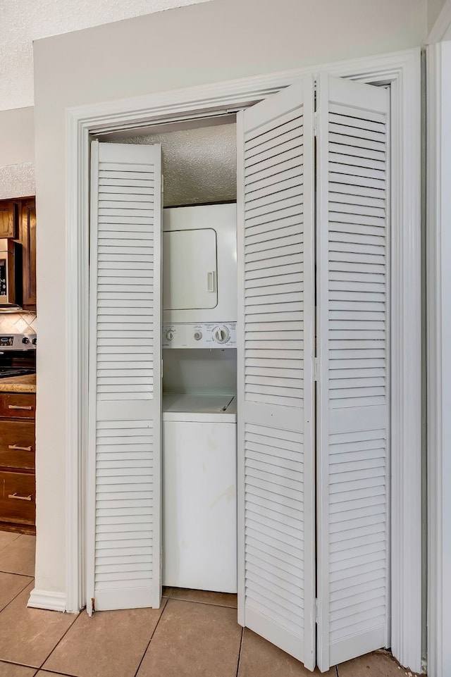 laundry area featuring stacked washer / drying machine, a textured ceiling, and light tile patterned floors