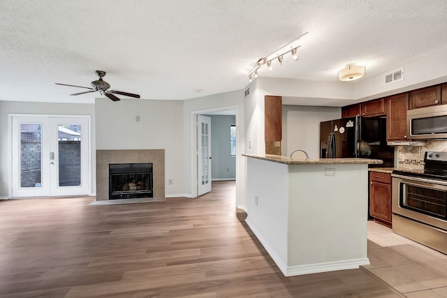 kitchen with appliances with stainless steel finishes, a fireplace, backsplash, a textured ceiling, and light hardwood / wood-style flooring