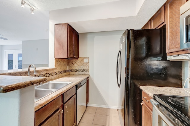 kitchen with light tile patterned floors, sink, stainless steel appliances, tasteful backsplash, and light stone counters