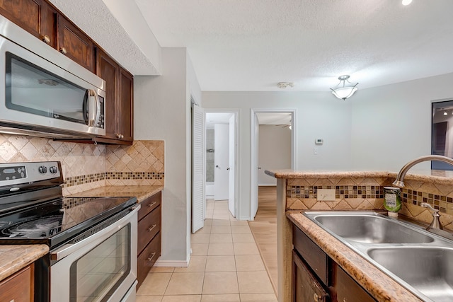 kitchen featuring sink, a textured ceiling, light tile patterned floors, appliances with stainless steel finishes, and backsplash